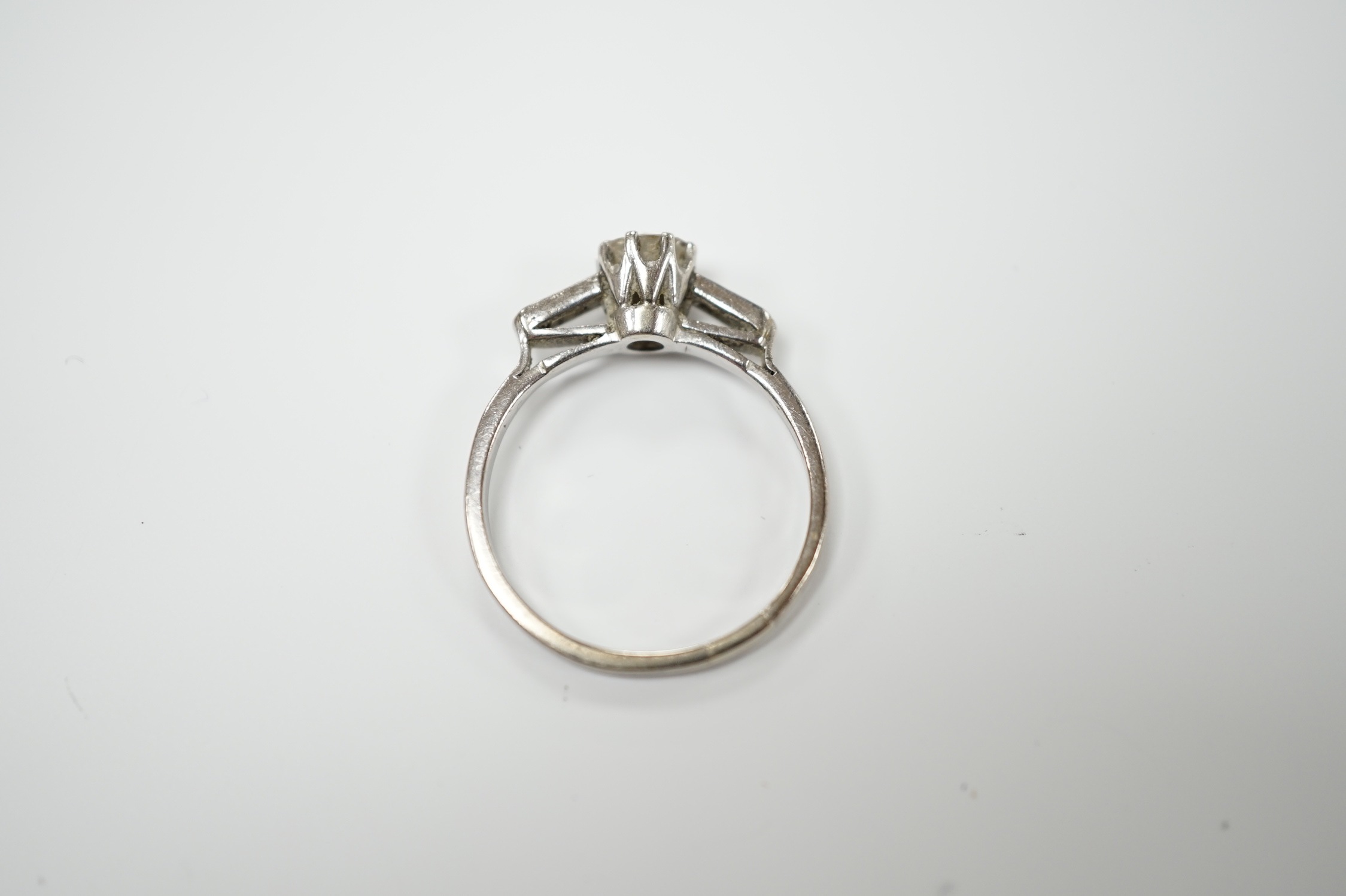 A white metal and single stone diamond set ring, with two stone baguette cut diamond set shoulders, size O, gross weight 2.3 grams, stone diameter 5.2mm.